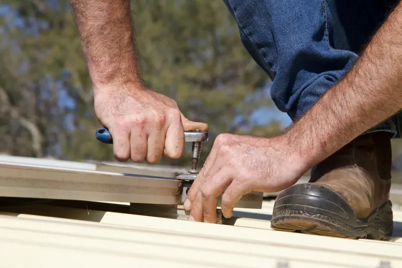 A roofer's hands tightening a screw on a cream metal roof