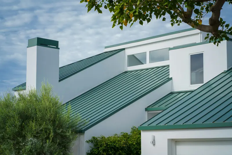 Green long-run roofs and flashings on a white house, seen from the ground
